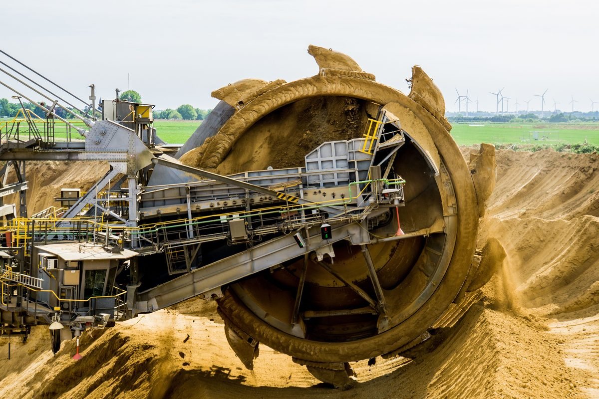 Surface mining equipment operating with wind turbines visible on the horizon
